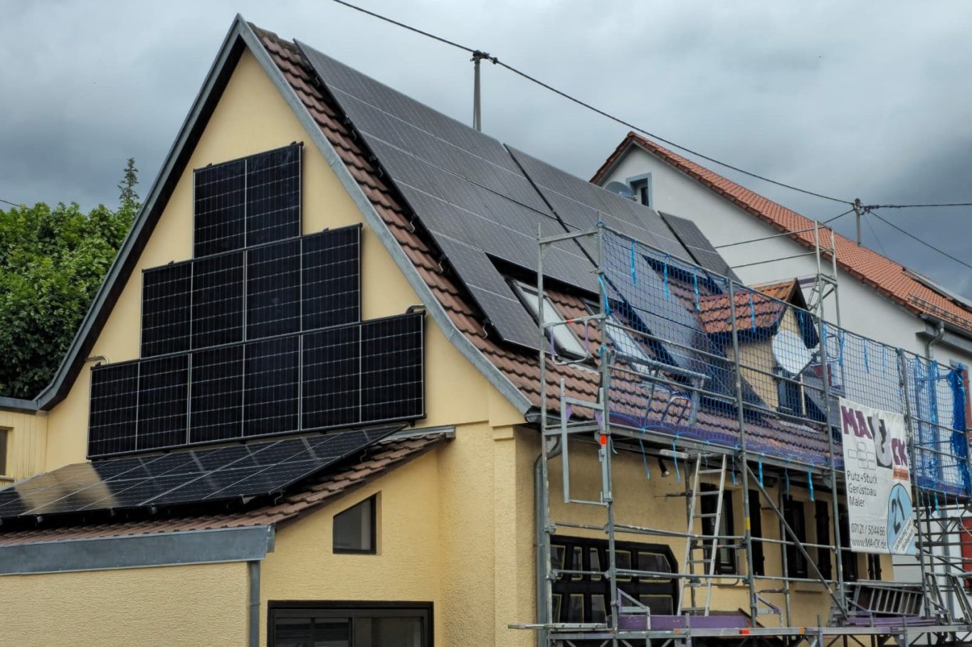 Haus mit Solarpanelen und Baustellengerüst, unter bewölktem Himmel.