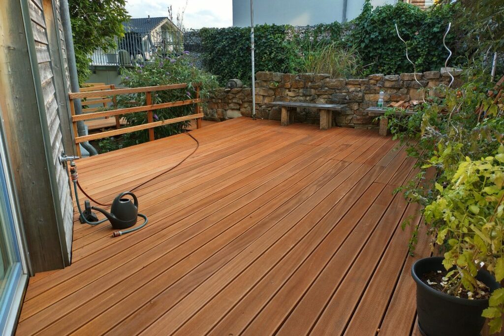 Hölzerne Terrasse mit Pflanzen und einer Steinmauer im Hintergrund.