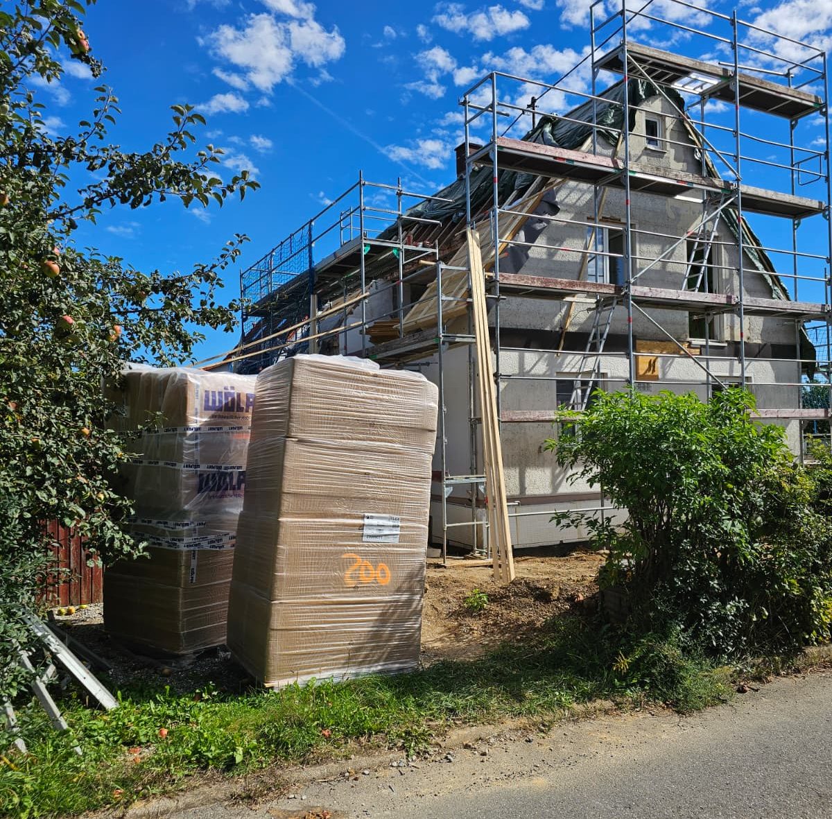 Baustelle eines Hauses mit Gerüst und Baustellenmaterial im Vordergrund.
