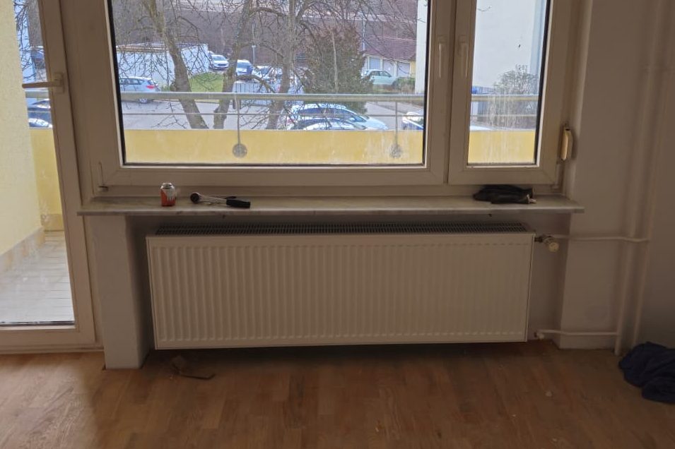 Heizkörper unter einem großen Fenster mit Blick auf einen Balkon.